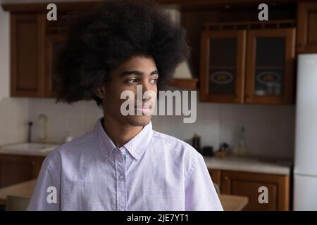 Serio e pensivo ragazzo africano in piedi in cucina domestica fissando da parte Foto Stock