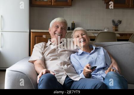 Le coppie più anziane si rilassano sul divano ridendo i canali di commutazione godersi il film Foto Stock