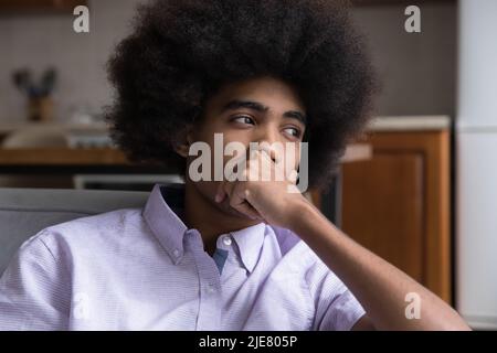 Il ragazzo adolescente africano pensivo profondo nei pensieri si siede sul divano Foto Stock