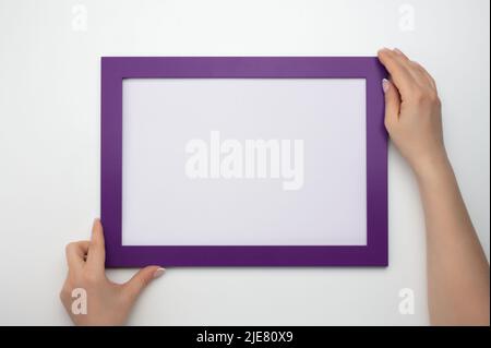 Telaio di supporto. Foto Mockup. Le mani della donna tengono la cornice viola. Per il design di cornici e poster. Dimensione cornice A4. Isolato su bianco. Cornice fotografica vuota Foto Stock