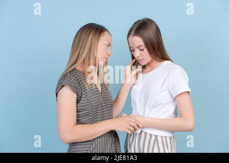 La mamma sostiene moralmente la figlia triste adulta che ha problemi, su sfondo blu. La donna caucasica fornisce assistenza psicologica ad una ragazza vestita con abiti casual. Concetto di aiuto per la famiglia Foto Stock