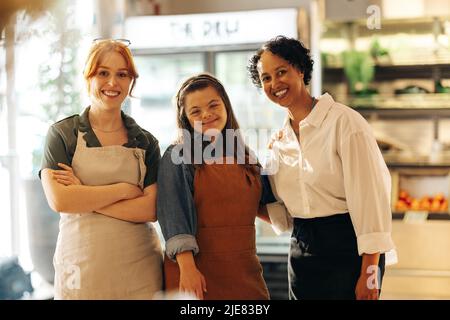 I lavoratori al dettaglio sorridono alla macchina fotografica mentre si trovano in un negozio di alimentari. Gruppo di tre donne diverse che lavorano insieme in un successo s. Foto Stock