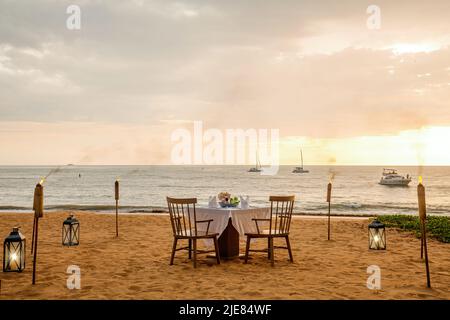 Romantica cena al tramonto sulla spiaggia. Tavolo luna di miele per due con cibo di lusso, bicchieri di champagne drink nel ristorante con vista mare e yacht Foto Stock
