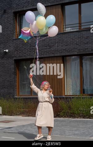 Donna in capelli colorati cammina con un'armatura di palloncini e beve una bevanda rinfrescante Foto Stock