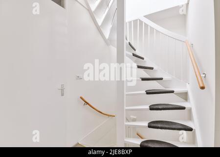 Da sopra di una stretta scalinata a chiocciola con scale bianche e ringhiera a muro all'interno di un moderno appartamento Foto Stock