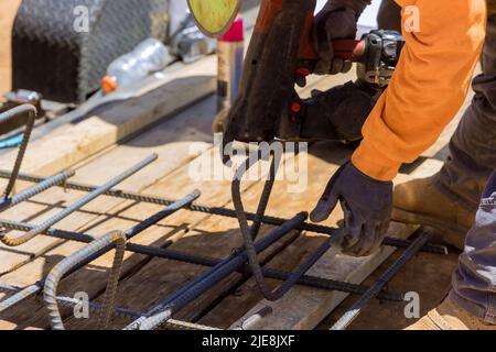 Utilizzando un attrezzo di legatura per barre di armatura, il lavoratore di costruzione attorciglia le barre di acciaio con le barre metalliche Foto Stock