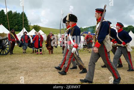 I membri del Reggimento di Devereaux (a sinistra) eseguono un saluto come membri della truppa Whinyates Rocket della Royal House Artillery (a destra) sfilano intorno al terreno del festival durante il festival di storia di Chalke Valley a Broad Chalke, vicino Salisbury, Wiltshire. Data foto: Domenica 26 giugno 2022. Foto Stock