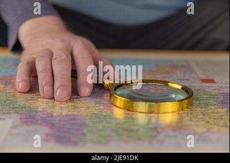 Un uomo tiene una lente d'ingrandimento in mano sopra una mappa. Uomo di mezza età con una lente d'ingrandimento in una cornice d'oro. I nomi sono scritti in ucraino. Foto Stock