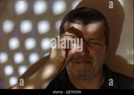 Un uomo che imita con la mano una lente d'ingrandimento. Ritratto di un uomo di mezza età contro un muro. Un disegno chiaro ed ombra di figure ripetitive sulla parete AN Foto Stock