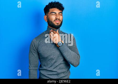 Uomo arabo con barba che indossa un maglione di dolcevita che tocca il collo doloroso, mal di gola per influenza, coagulo e infezione Foto Stock