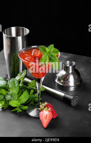 Cocktail freddo estivo di fragole mojito, margarita, daiquiri in un bicchiere martini su sfondo scuro con set barman Foto Stock