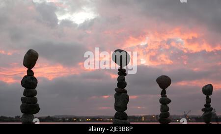 Bilanciamento della roccia contro cielo nuvoloso e drammatico al tramonto. Pila di pietre in equilibrio, piramide stabile nel crepuscolo rosa della sera. Nuvolosità al tramonto dall'acqua marina dell'oceano. Concetto di buddismo. Foto Stock