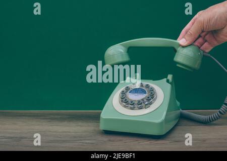 Un telefono britannico d'epoca o retrò degli anni Settanta e una mano che solleva il ricevitore per rispondere a una chiamata Foto Stock