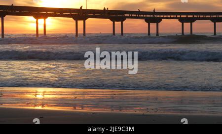 Silhouette di persone che camminano, molo su pali in acqua di mare. Onde oceaniche, cielo drammatico al tramonto. California costa estetica, spiaggia o spiaggia vibrazione al tramonto. Estate stagcape a San Diego vicino Los Angeles Foto Stock