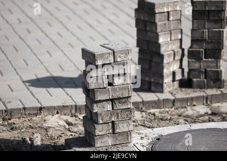 Vista delle nuove lastre di pavimentazione e dei blocchi di calcestruzzo nella giornata estiva presso il cantiere. I blocchi di pietra si trovano nella pila. Riparazione di quadrate e marciapiedi. Restauro del manto stradale. Foto Stock