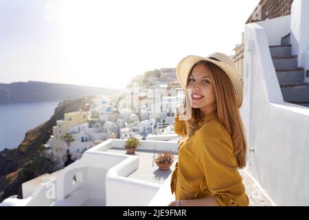 Tramonto a Santorini. Romantica giovane donna attraente godendo il paesaggio del villaggio di Oia a Santorini, Grecia. Guardando la fotocamera. Foto Stock