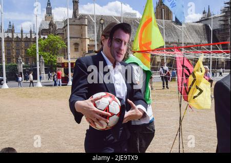 Londra, Regno Unito. 26th giugno 2022. Un protettore vestito come presidente francese Emmanuel Macron. Estinzione gli attivisti della ribellione vestiti da G7 leader hanno giocato una partita di calcio in Piazza del Parlamento contro i “Paesi indebitati”, i cui giocatori sono stati oppressi dal debito incatenato alle gambe, con la partita truccata a favore del G7 da un “arbitro banchiere”. L’azione è stata parte della protesta del giorno in cui si chiedeva che il G7 annulli il debito dei paesi del Sud del mondo, che sta costringendo le nazioni ad estrarre combustibili fossili per ripagare i debiti. Credit: Vuk Valcic/Alamy Live News Foto Stock