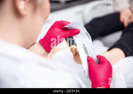 I chiropodisti sconfezionano una lama per bisturi dalla confezione sterile Foto Stock