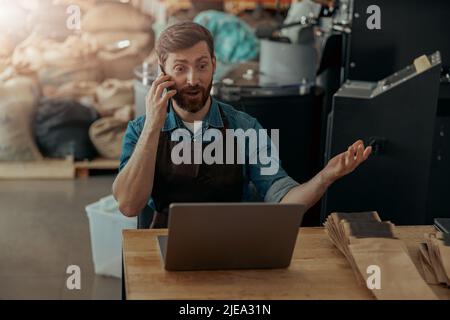 Il proprietario di affari che parla con il cliente mentre siede nella propria piccola fabbrica di caffè Foto Stock