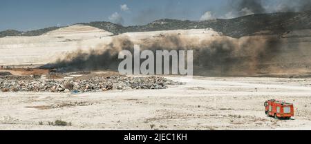 Lotta antincendio in un cantiere di pneumatici. Colpo panoramico di rifiuti con camion antincendio e macchinari movimento terra Foto Stock