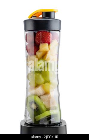 Il frullatore a immersione è pieno di fragole, ananas, banane e kiwi e su sfondo bianco. Foto Stock