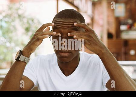 stanco uomo interrazziale scuro pelle in occhiali toccare e strofinare gli occhi, sensazione di dolore. Problema di visione Foto Stock