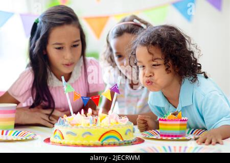 Festa di compleanno dei bambini. I bambini festeggiano con torte colorate e regali. Piccolo ragazzo curly soffiando candele e l'apertura di regali di compleanno. Foto Stock