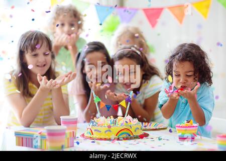 Festa di compleanno dei bambini. I bambini festeggiano con torte colorate e regali. Piccolo ragazzo curly soffiando candele e l'apertura di regali di compleanno. Foto Stock