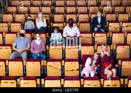 Adulti con bambini in maschere protettive che guardano il gioco a teatro Foto Stock