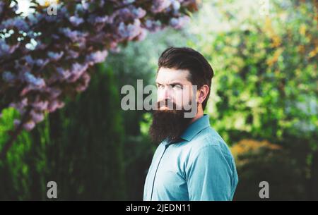 Uomo ispanico di successo in giardino di primavera. Ritratto di un giovane uomo bello, modello di moda, con acconciatura formale pensiero in primavera parco, vestendo Foto Stock