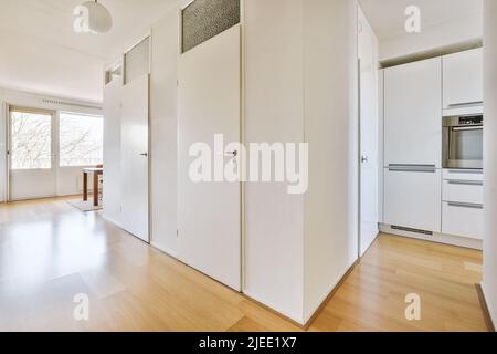 Hall con pareti bianche e porte che conduce a una cucina con pavimenti in parquet in un moderno appartamento Foto Stock