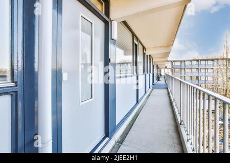 Lungo balcone con ringhiere bianche lungo un edificio di appartamenti blu in una giornata di sole Foto Stock