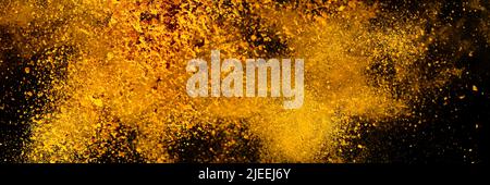 Esplosione, schizzi di curcuma su sfondo nero. India Seasoning. La polvere arancione della radice curmerica. Foto Stock