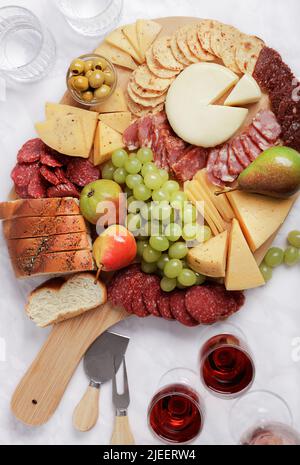 Piatto di formaggi. Fette di formaggio su piatti, uva, mele, pere, pane, salsiccia, salame, olive, olive nere, biscotti, spuntini, cracker, vino. Superiore Foto Stock