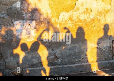 Ombre di danzanti su una vecchia parete al tramonto. Gruppo di ombre umane sullo sfondo del muro di pietra. Foto Stock