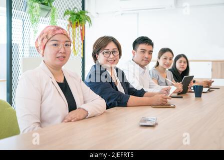 Ritratto di un gruppo di colleghi corporativi asiatici seduti insieme in una fila, in un ufficio moderno. Foto Stock