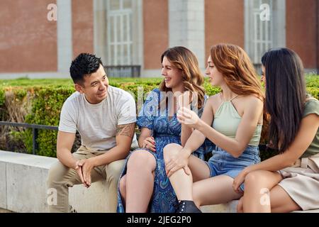 Gruppo di amici diversi che parlano mentre si rilassano e si godono il tempo insieme seduti all'aperto. Concetto di amicizia. Foto Stock