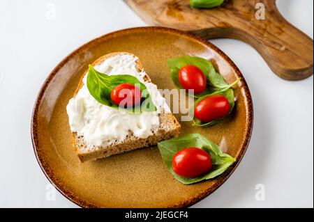 Piatto con pane con mozzarella e pomodoro ciliegia su foglia di basilico, tavola di legno su sfondo bianco. Foto Stock