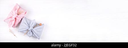 Banner Web con furoshiki natalizio che si avvolge sul tavolo bianco in legno. Concetto di zero rifiuti. Stile a disposizione piatta. Foto Stock