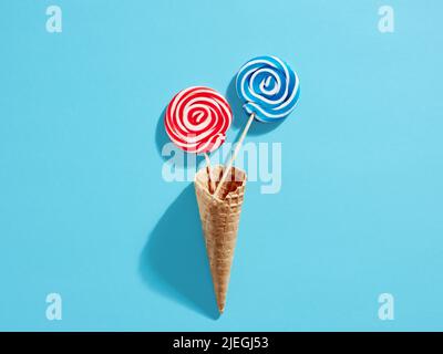 Colourful roteare intorno lecca caramelle in cialde gelato cono su sfondo blu. Foto Stock