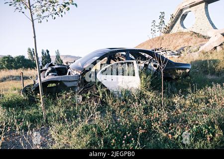 Discarica di auto, rottami di metallo. Primo piano di una vecchia auto abbandonata in un cortile con erba che germogliano all'interno e ciottoli troppo coltivati. Il sole si riflette Foto Stock