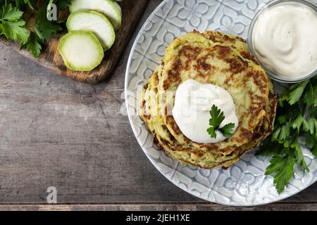 Frittelle di zucchine con salsa di yogurt su tavola di legno Foto Stock