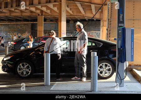 Persone che utilizzano un raro PlugNYC bordo marciapiede veicolo elettrico caricabatteria per ricaricare la loro auto elettrica a New York City.The rete pubblica EV è .. (vedere le informazioni) Foto Stock