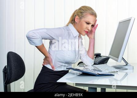 Eine junge Frau sitzt im Büro und hat Rückenschmerzen, Frau, 30, 35, Jahre, biondo, Foto Stock