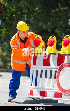 Ein Arbeiter überprüft die Baustellenabsperrung , Mann, 35, 40, Jahre, gelber Schutzhelm, Signalweste, schutzkleidung, Foto Stock