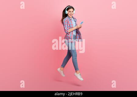 Foto a tutta lunghezza di buona signora positiva umore in wireless auricolare surf in telefono isolato su sfondo rosa Foto Stock