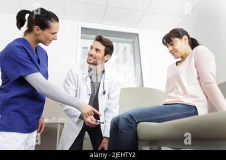 giovane medico di sesso maschile che controlla i riflessi del ginocchio della paziente femminile Foto Stock