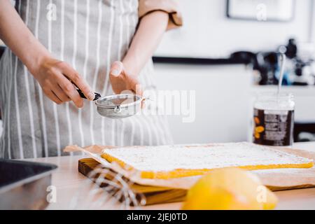 Cuochi le mani con setaccio piccolo per cuocere. Baker decorazione e spolverare torta o torta d'arancia con zucchero a velo. Sfondo cucina, fatta in casa e a mano Foto Stock