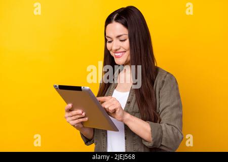 Foto di allegro bella bella giovane donna tenere mani guardare tablet sorriso isolato su sfondo di colore giallo lucido Foto Stock