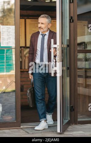 Uomo con borsa che tocca la porta lasciando l'edificio Foto Stock